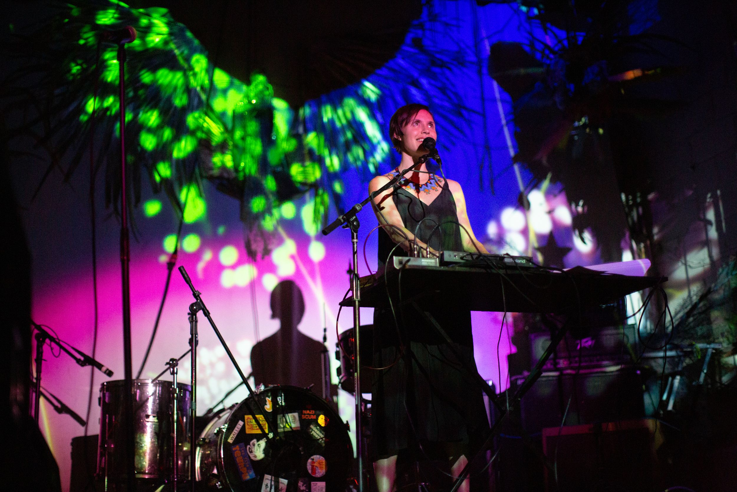 Concert performer plays keyboard on stage with vibrant green and blue lighting effects in the background.