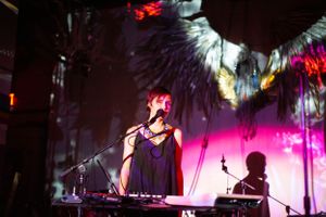 Live performance scene with silhouetted figures against bright pink stage lighting.