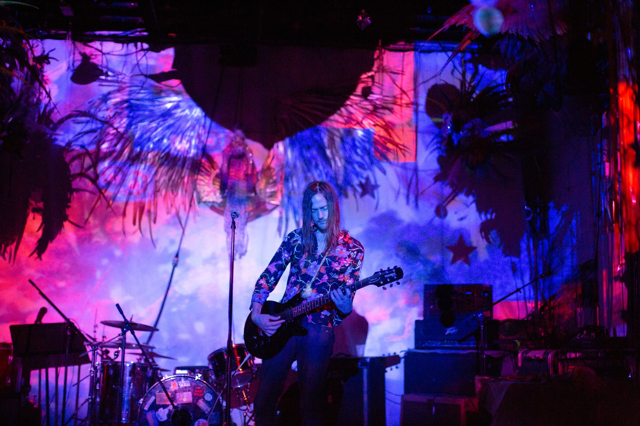 Colorful concert stage setup with palm tree silhouettes against pink and purple lighting effects.