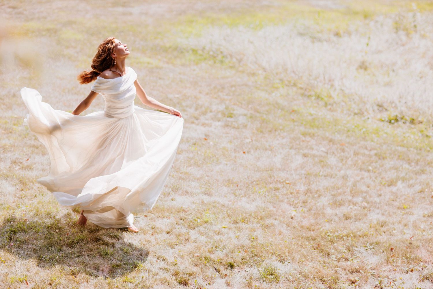 Woman in flowing white dress twirling in sunlit meadow.