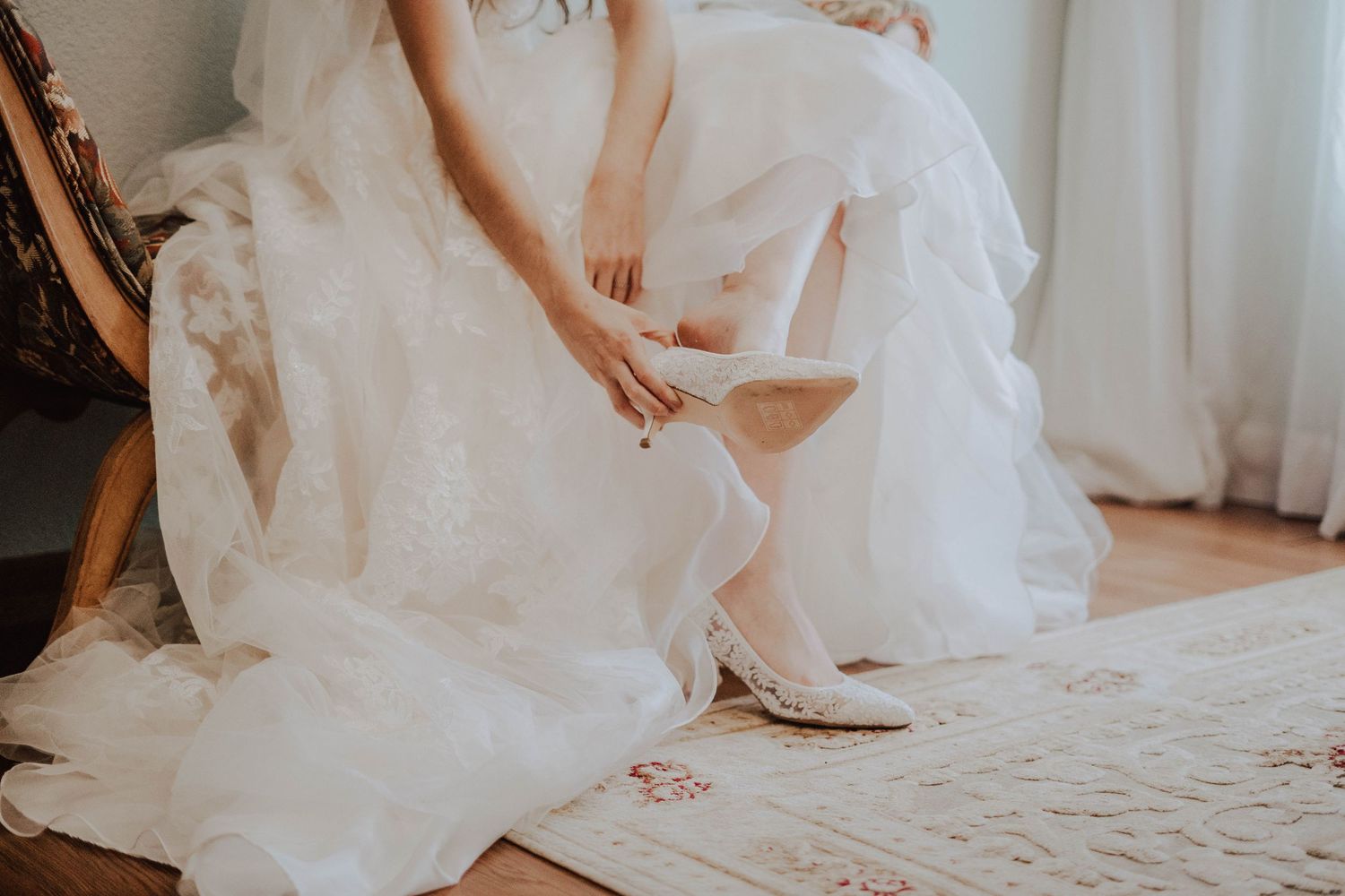 Bride wearing a white dress puts on lacy white shoes in the bridal suite at Casa Blanca at Brushy Creek