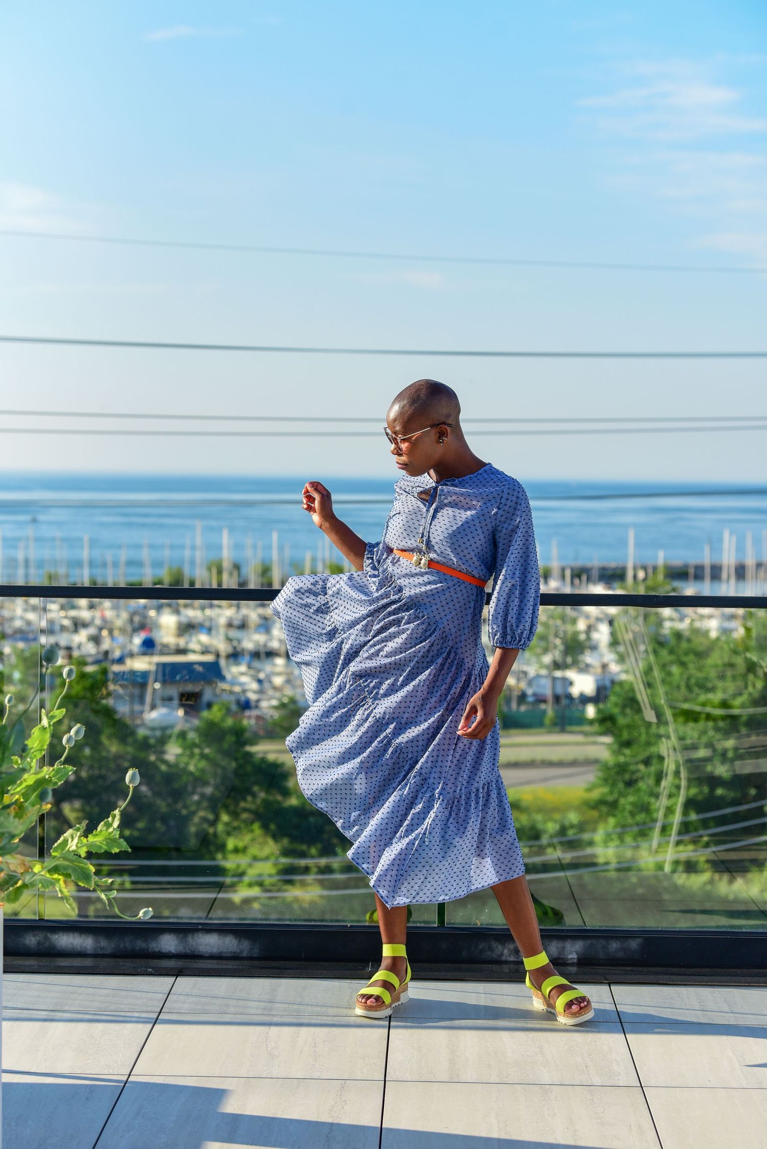 A blue gingham dress flows gracefully against a marina backdrop with yellow socks and sandals adding a playful pop of color.