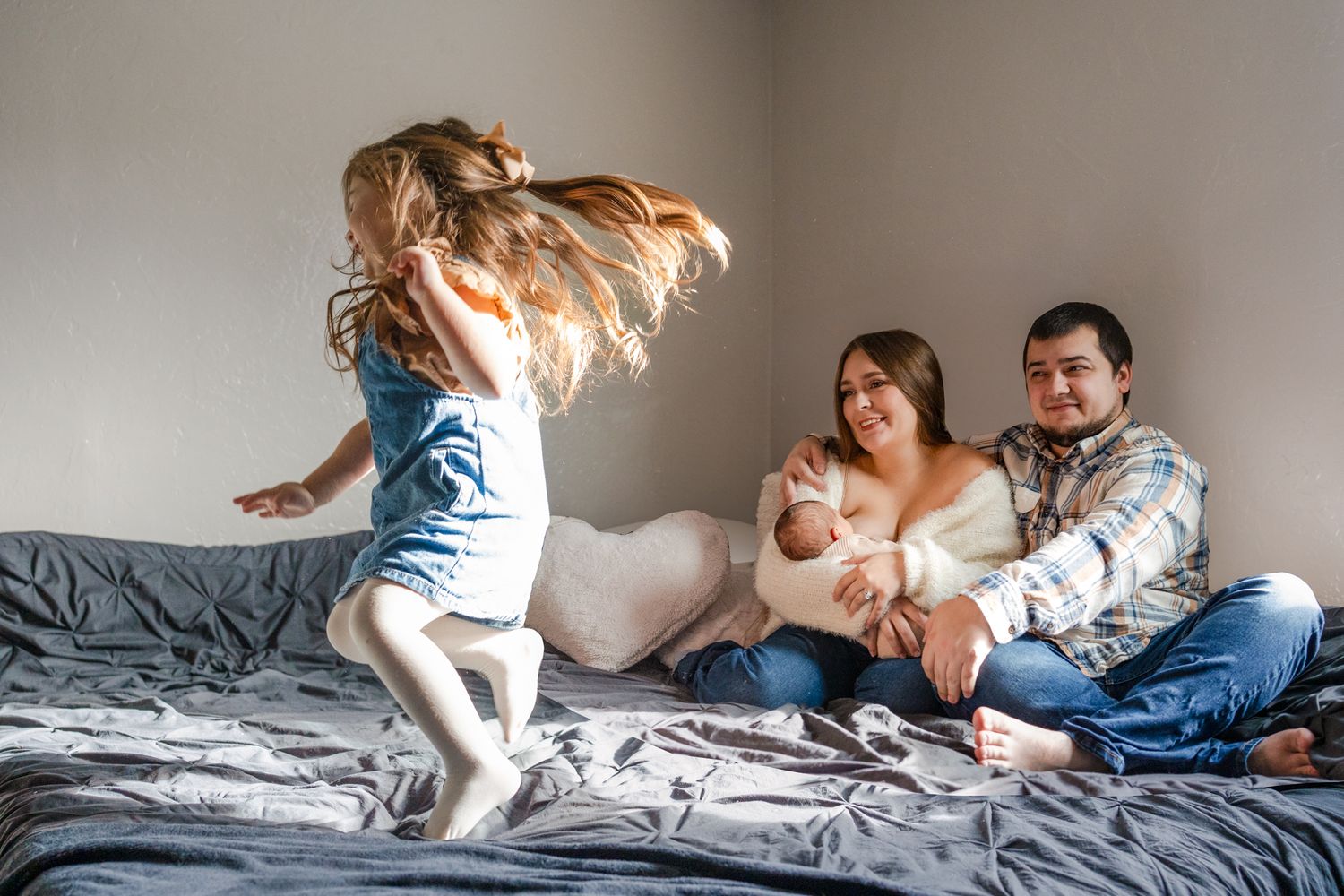 girl twirling on the bed with mom and dad with newborn son on the bed