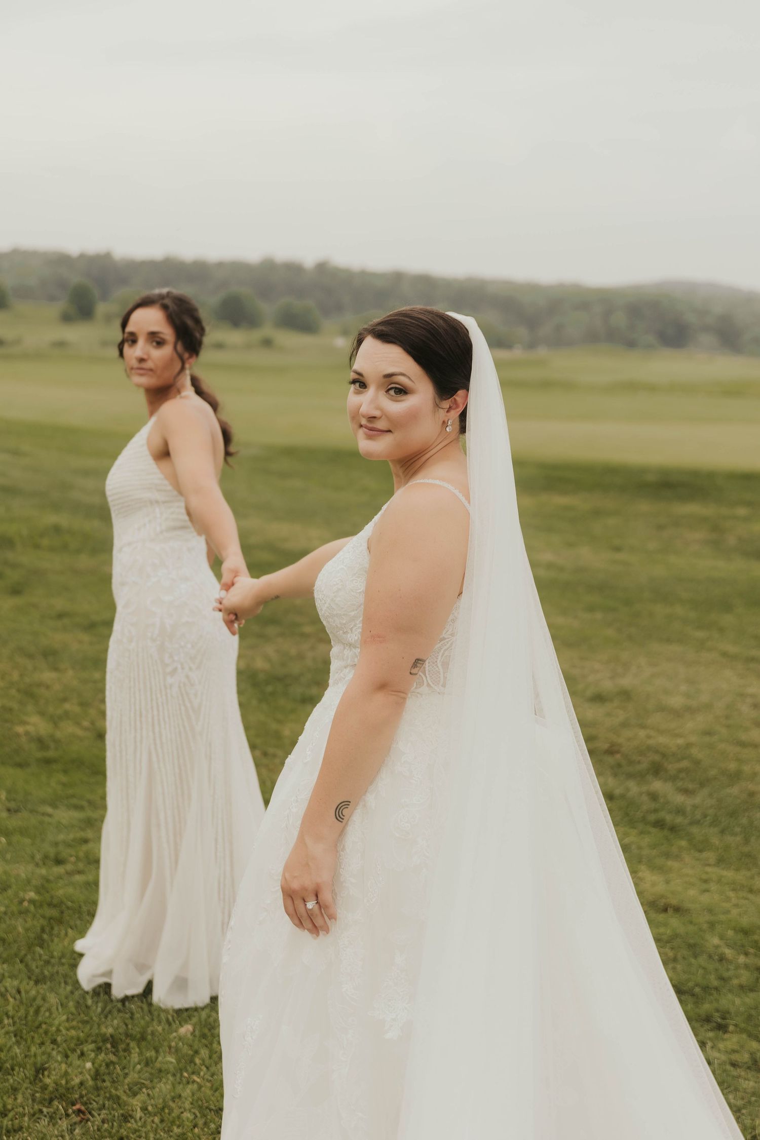 Wedding party in white dresses posing in a sunlit grassy field.