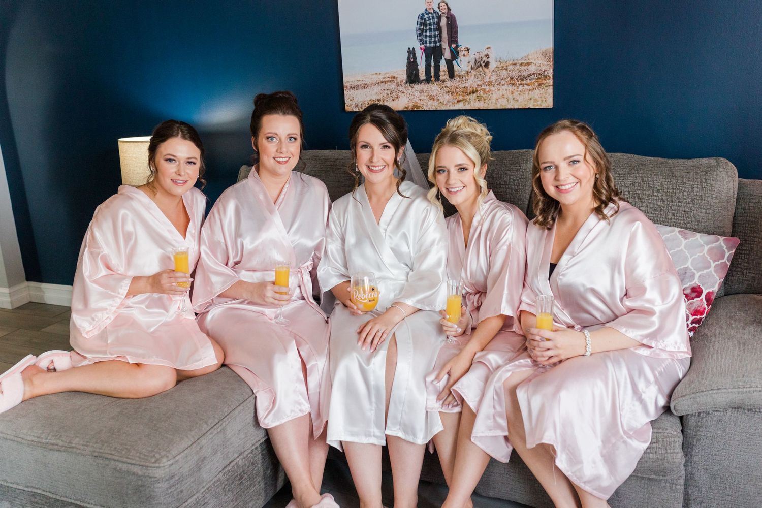 Bridal party relaxing on a gray couch in matching pink silk robes.