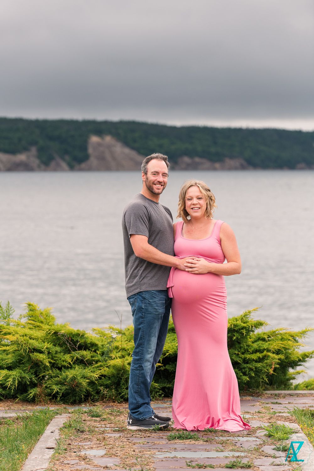 Maternity portrait with couple in casual wear against dramatic coastal landscape.