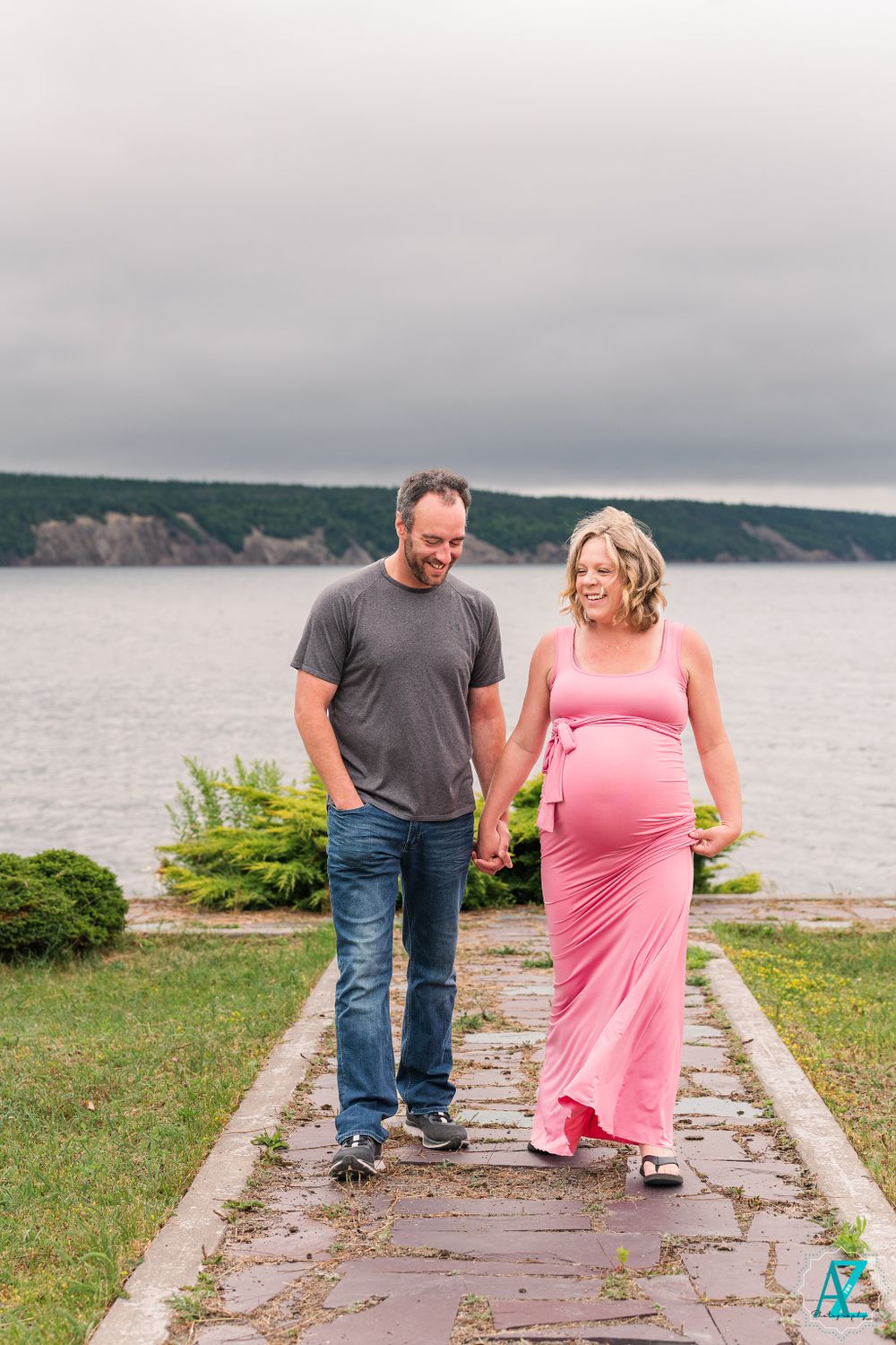 Couple walking on stone path during waterfront maternity photoshoot.