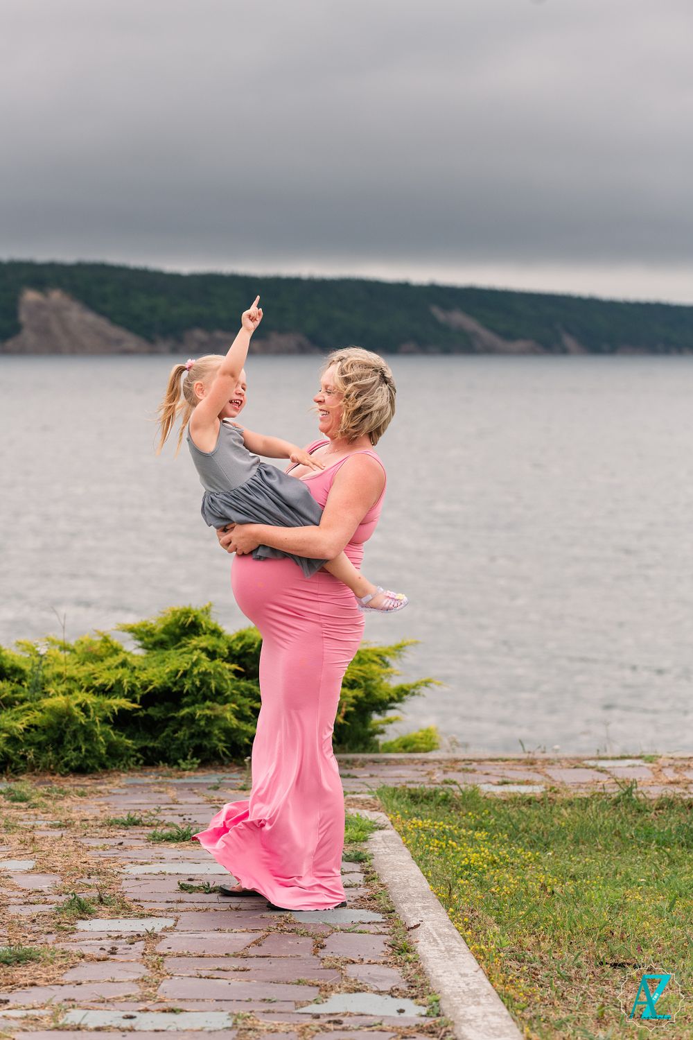 A joyful moment captured on a coastal path as figures share a playful interaction against a waterfront backdrop.