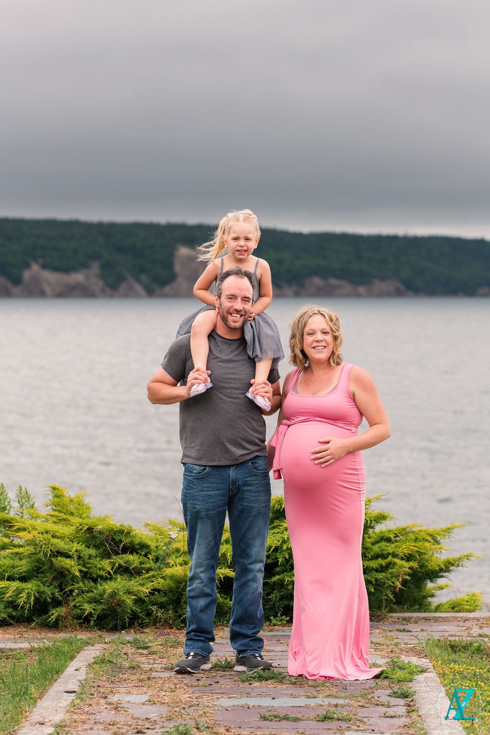 A happy family moment captured on a stone path with scenic coastal cliffs and water in the background.