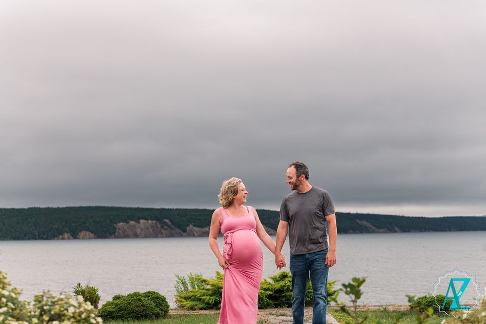 A couple shares a moment on a grassy overlook with a scenic coastal view in the background.