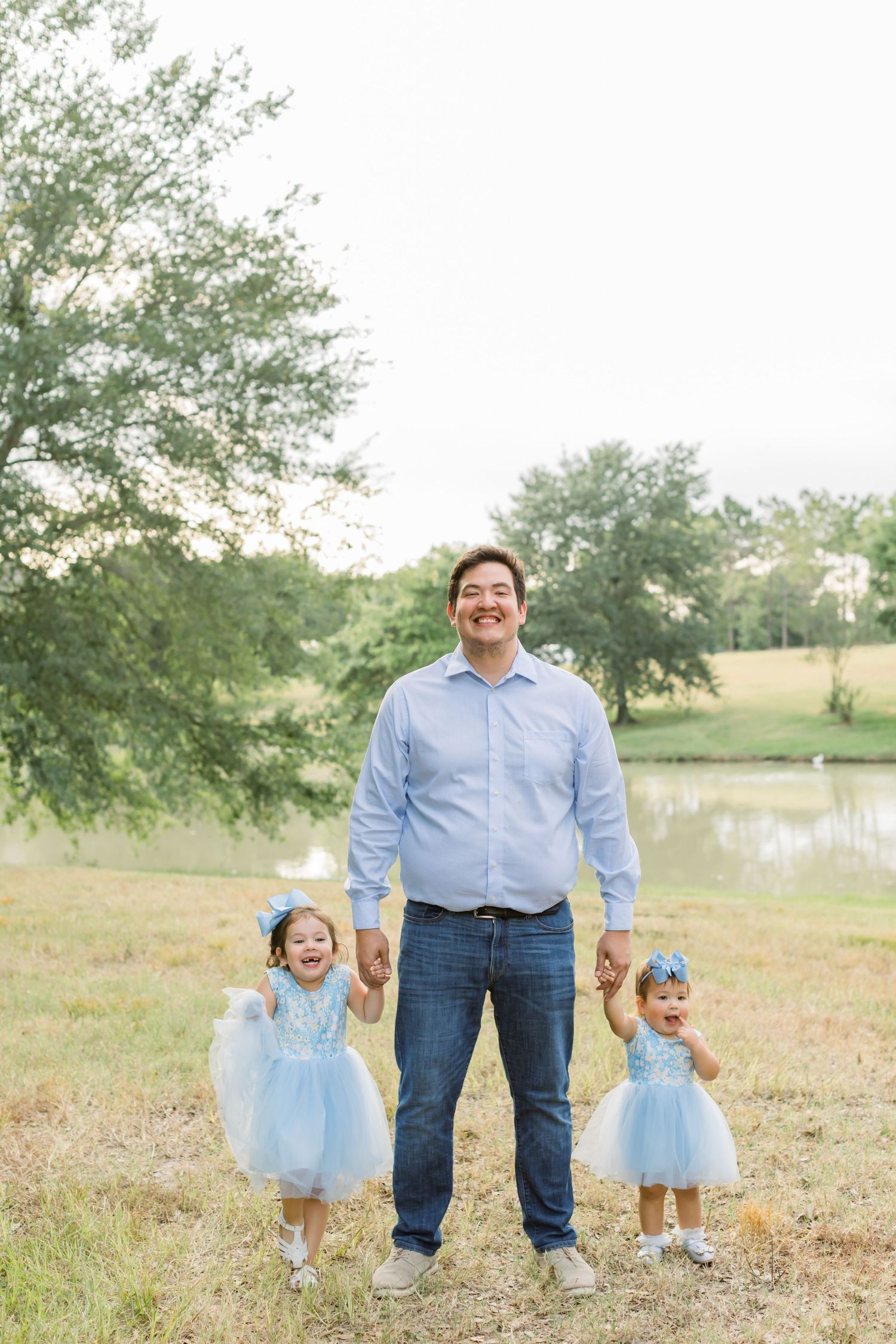 Young girls in blue tulle dresses holding hands and laughing outdoors with adult.