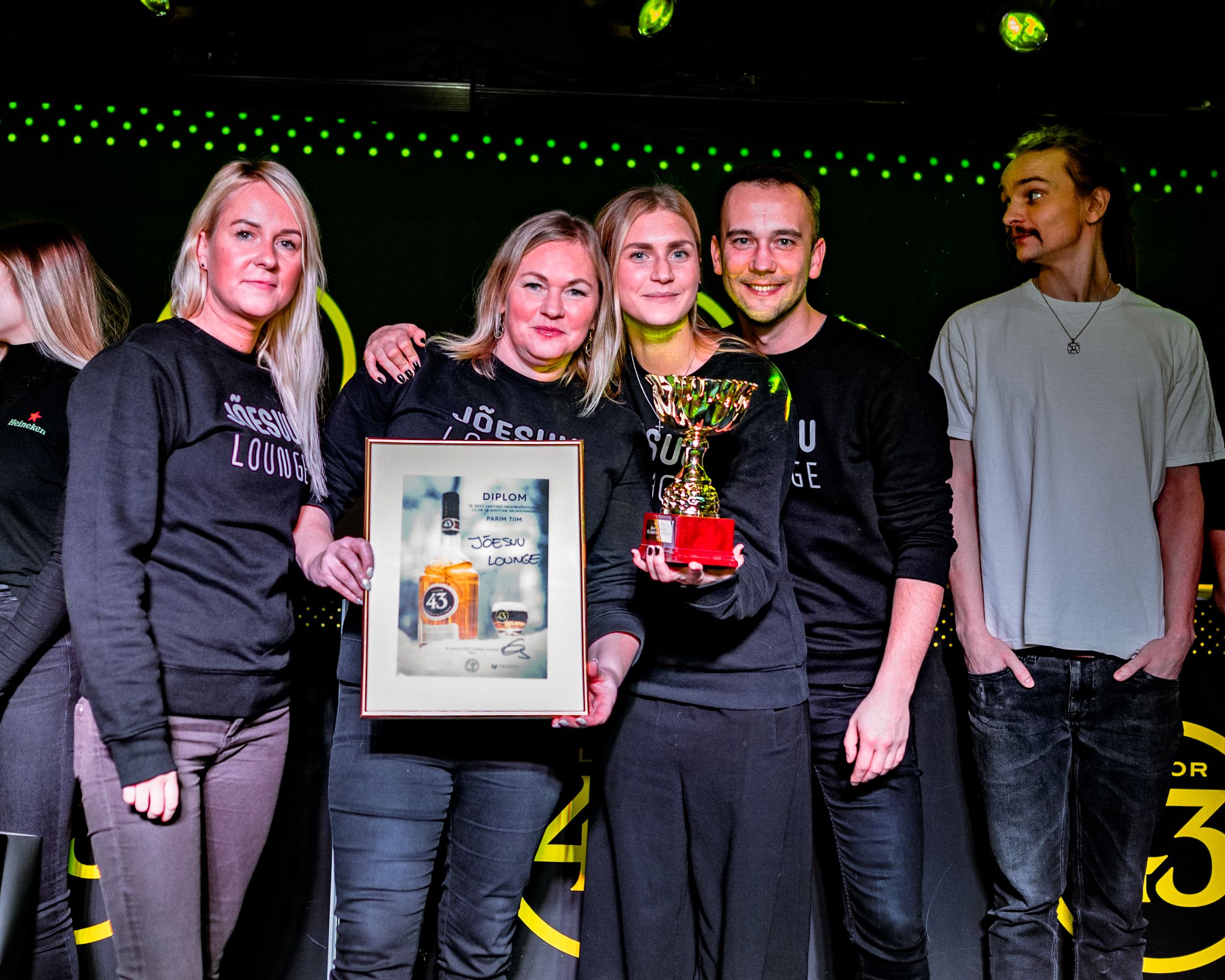 Award recipients pose together holding framed certificates and trophies at a nightclub celebration.