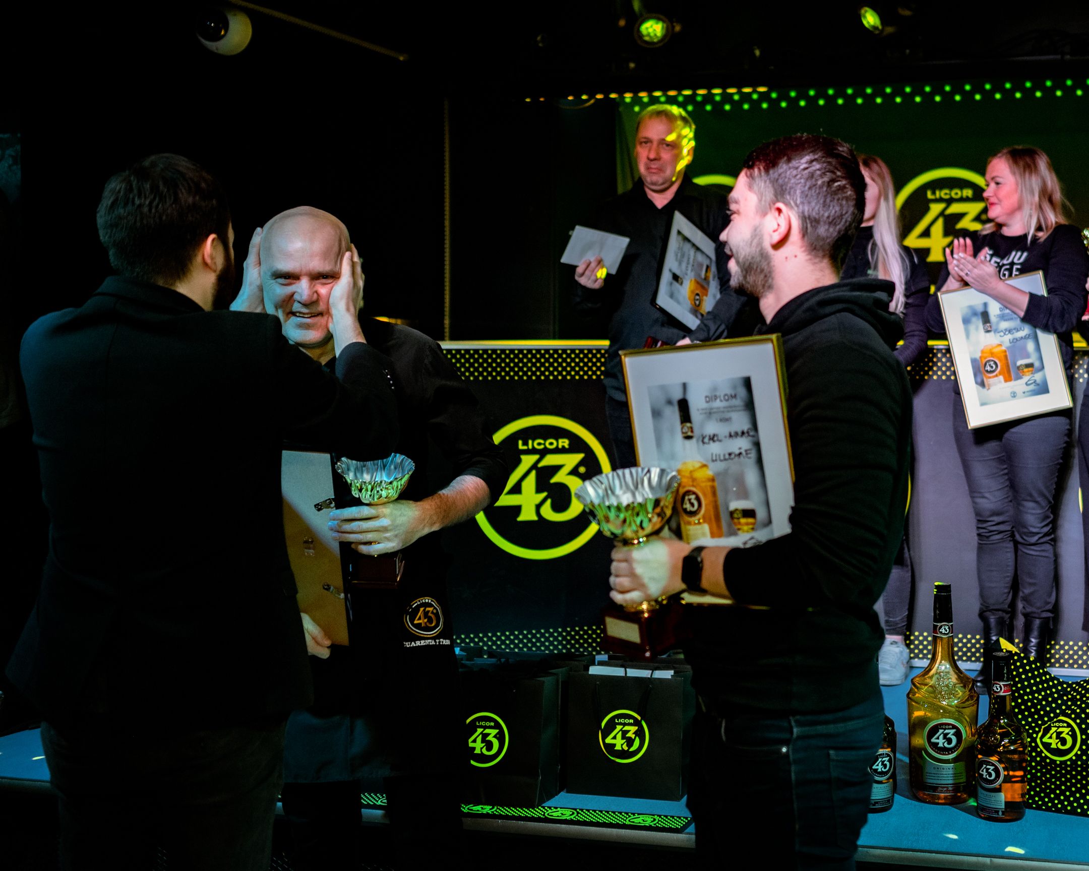 Group celebrates during an awards ceremony on stage with certificates and drinks.