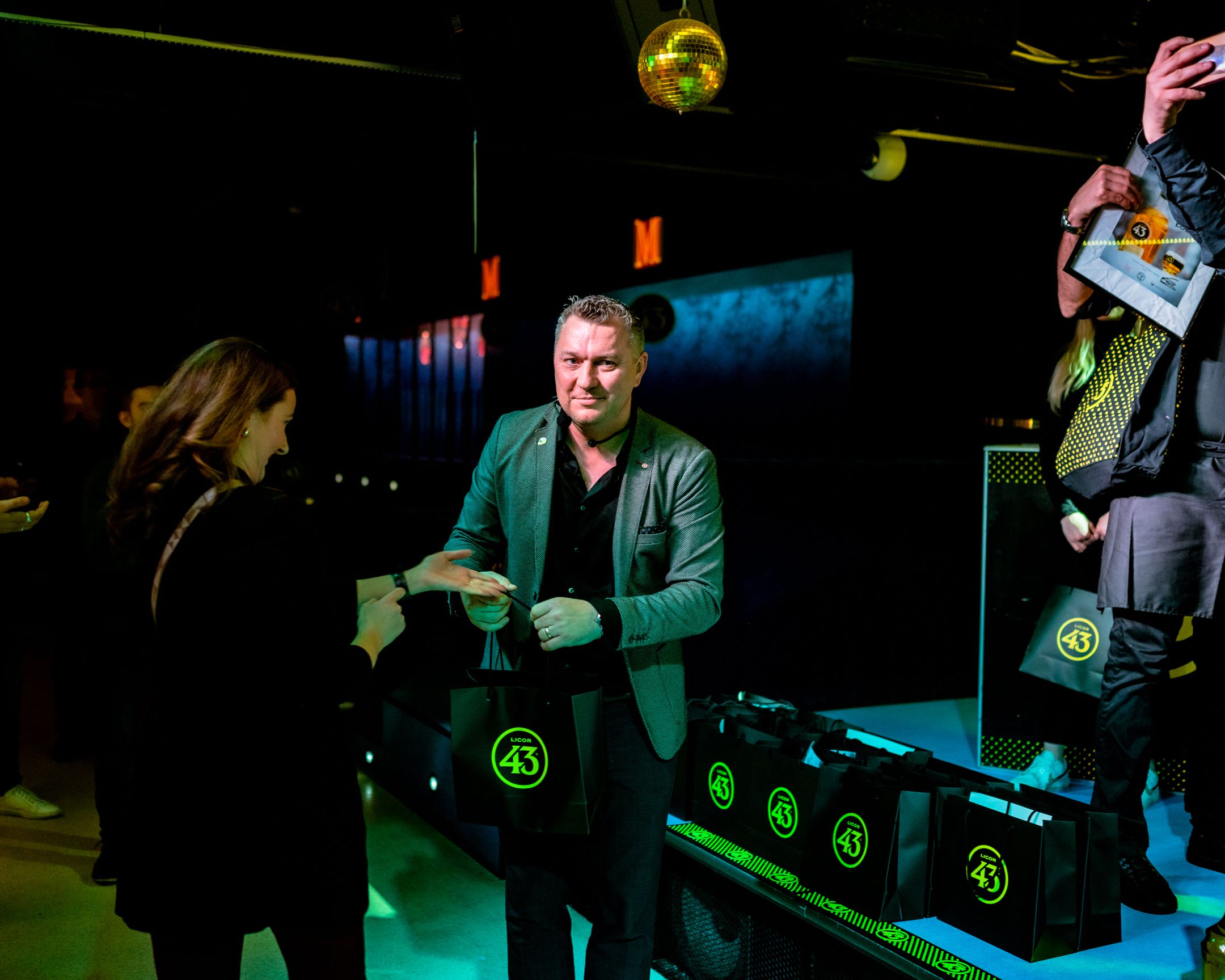 Person in green jacket at nightclub awards event with lighting effects.