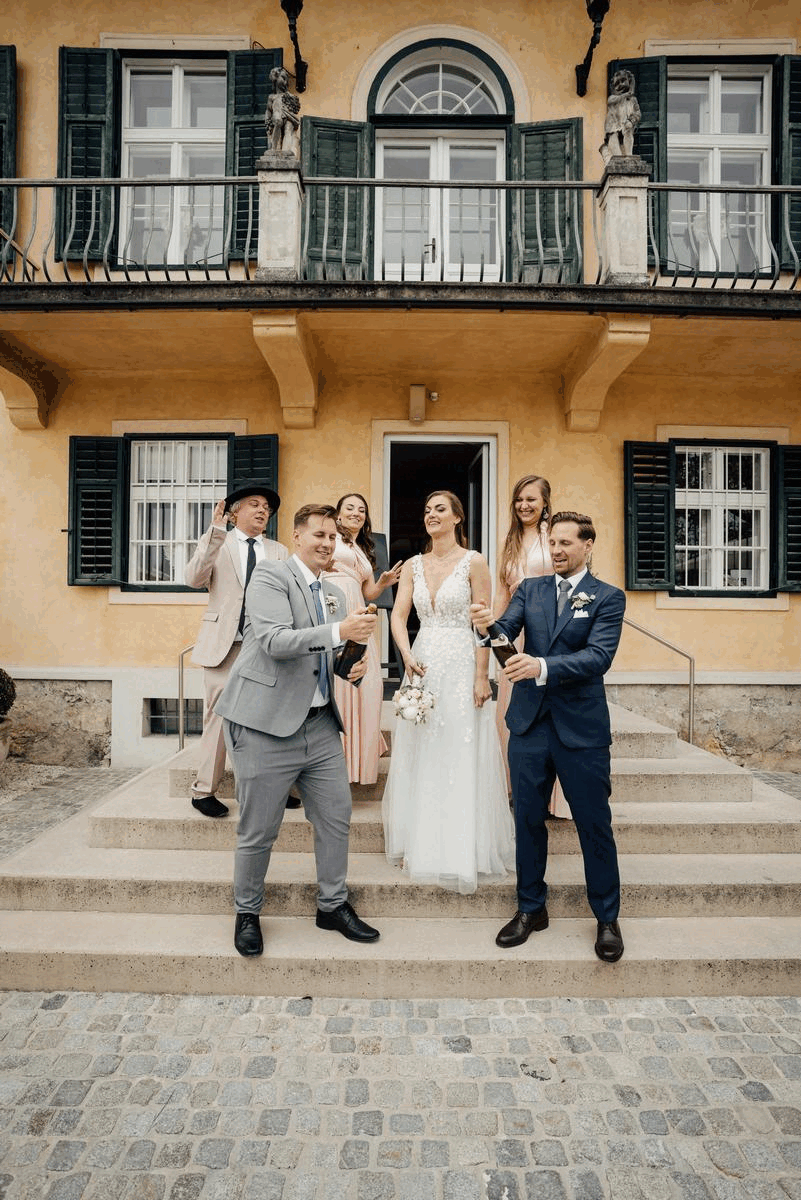 Hochzeitspaar verspritzt Sekt mit Trauzeugen vor Aiola im Schloss St. Veit