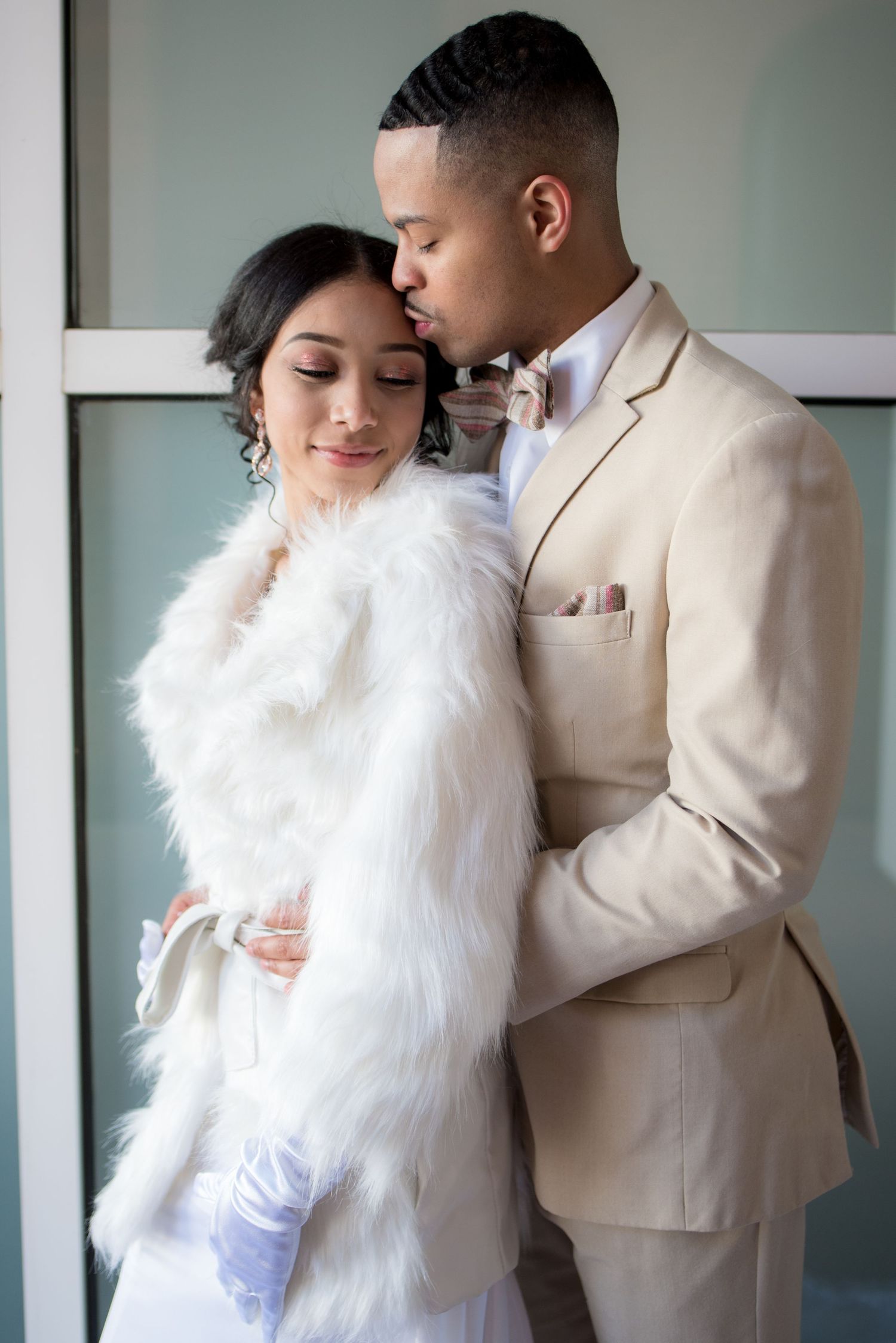 An elegant couple in light formal wear share an intimate moment indoors.