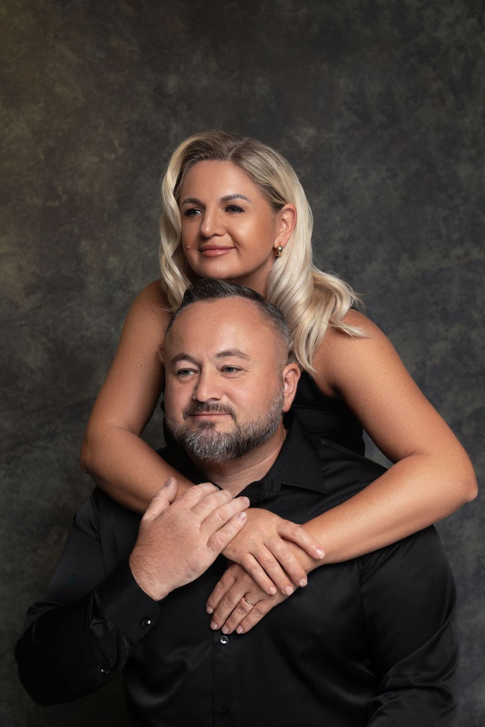 Professional studio portrait of a couple embracing against a dark textured background.