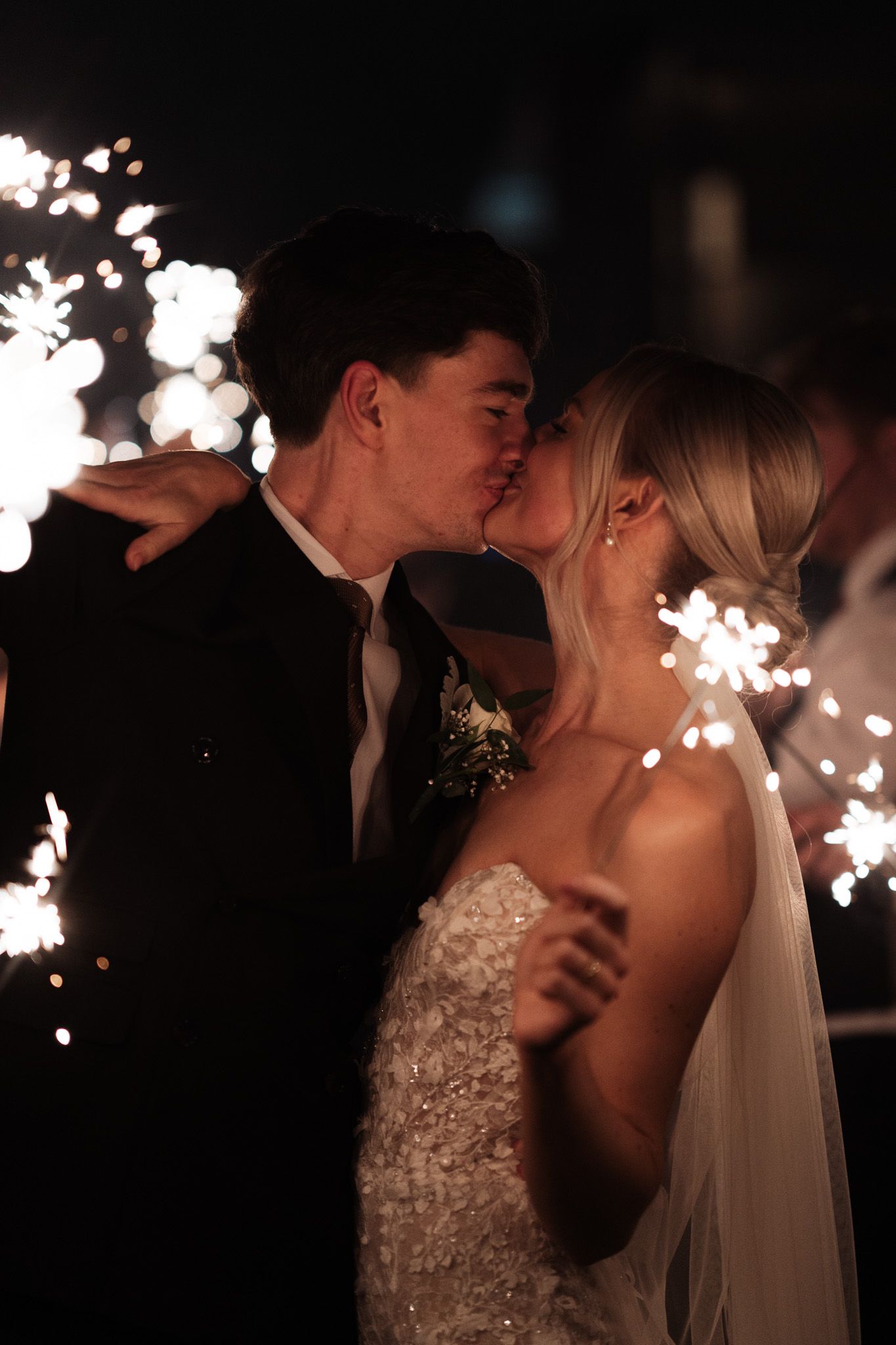 Romantic couple sharing a kiss surrounded by sparkling wedding sparklers at night.