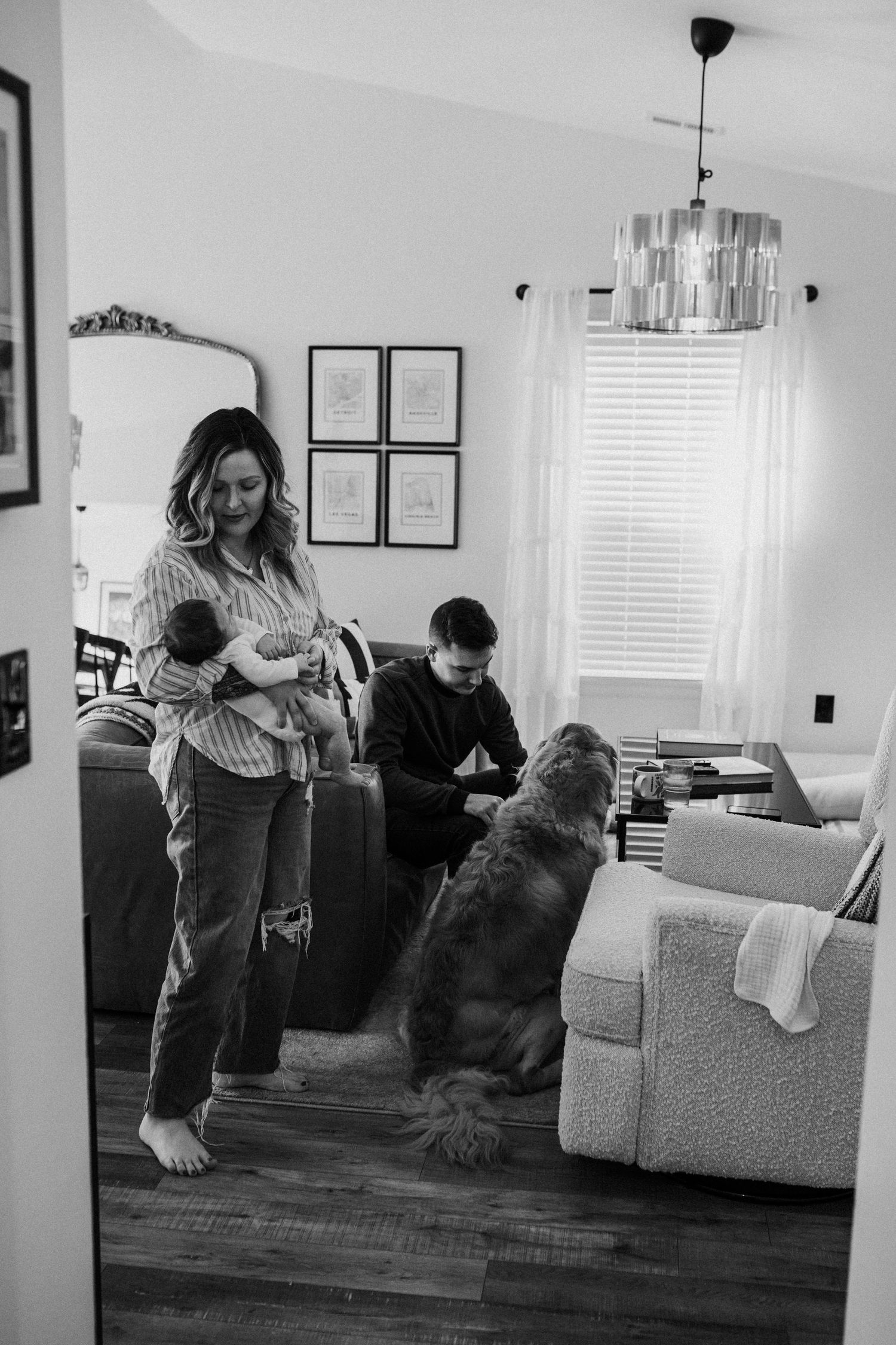 black and white portrait of mother holding baby at home with dad and dogs in the background