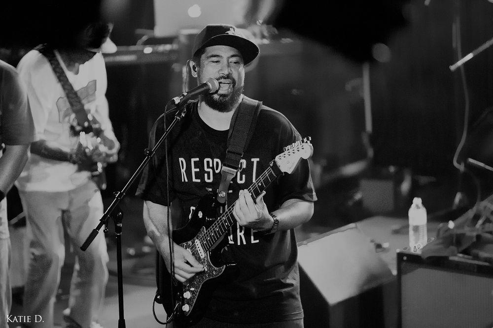 Guitarist in black shirt singing passionately into microphone during live band performance.