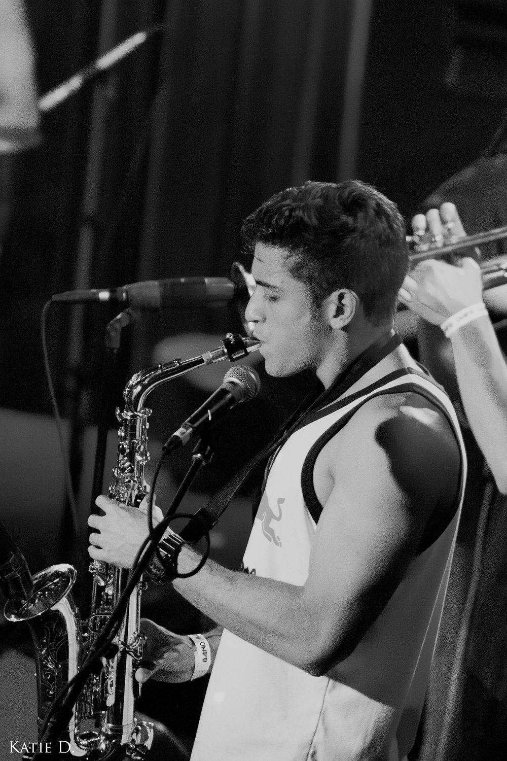 Young musician playing saxophone on stage in black and white concert photo.