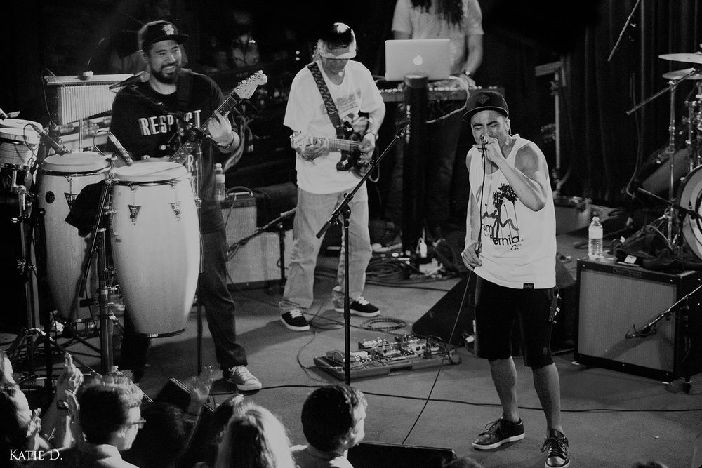 Black and white wide shot of a full band performing live on stage before an audience.