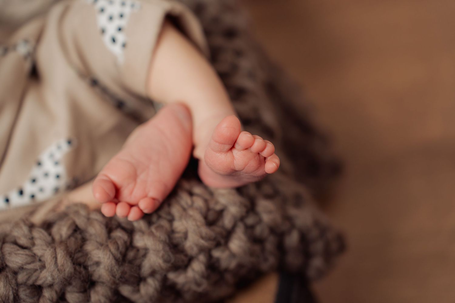 Close-up of tiny baby feet resting on chunky knit brown blanket.