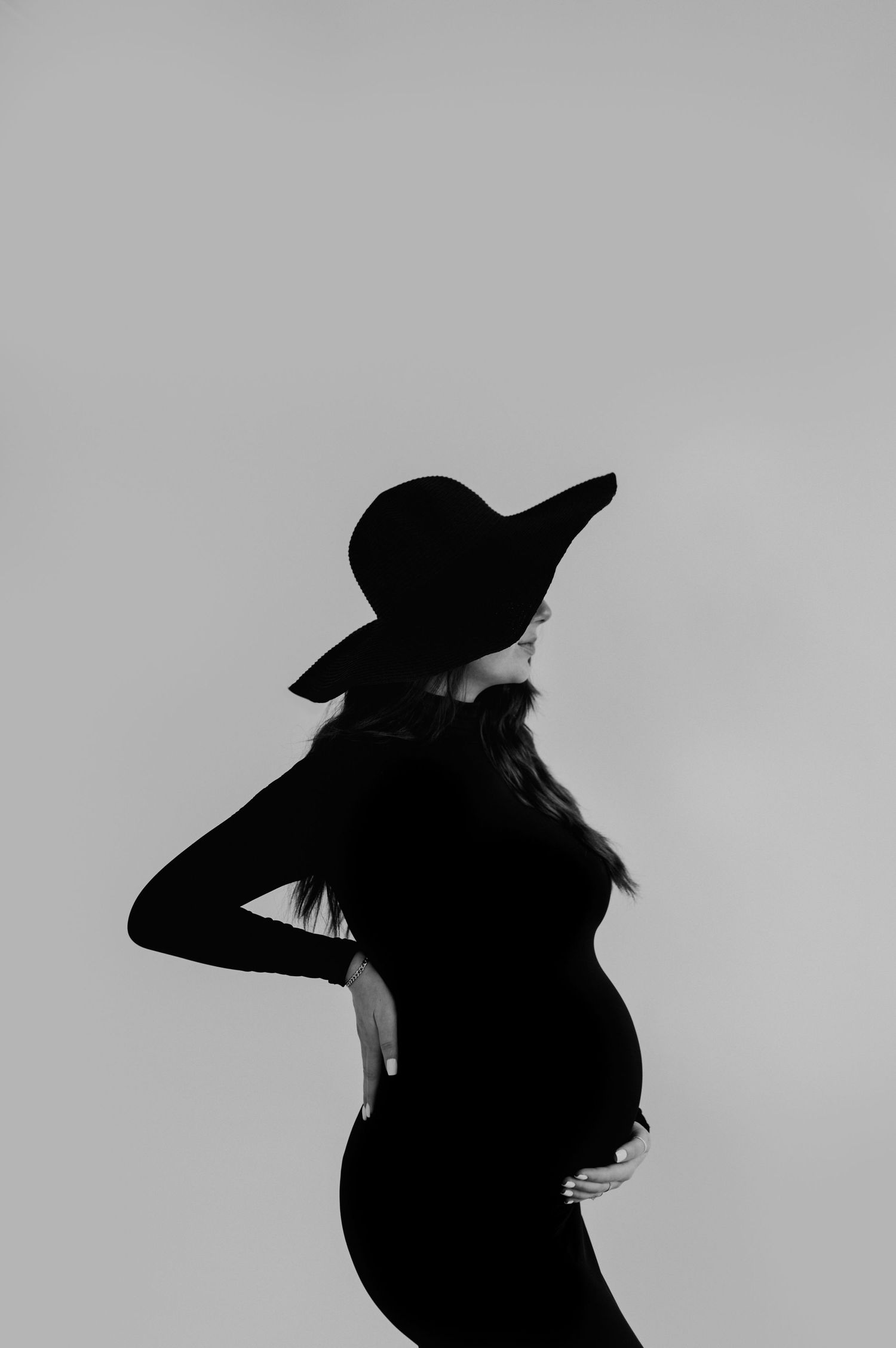 A silhouette of an expectant mother in a wide-brimmed hat against a light background.