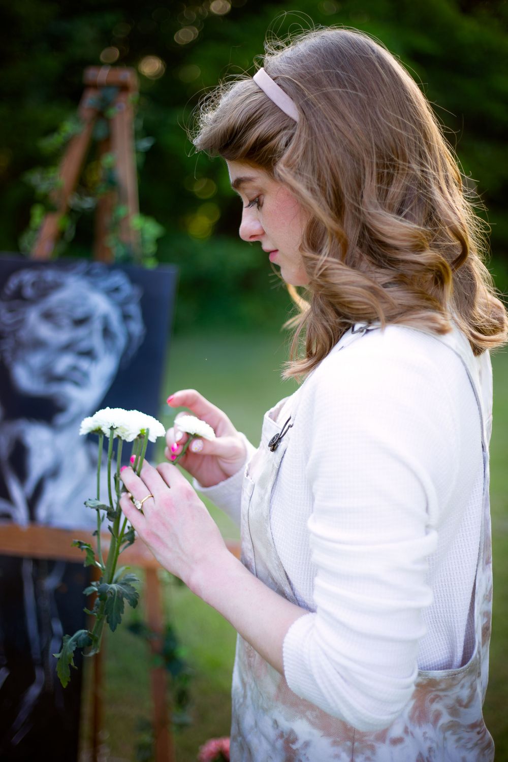 Artist examining delicate white flowers while painting outdoors in a garden setting.