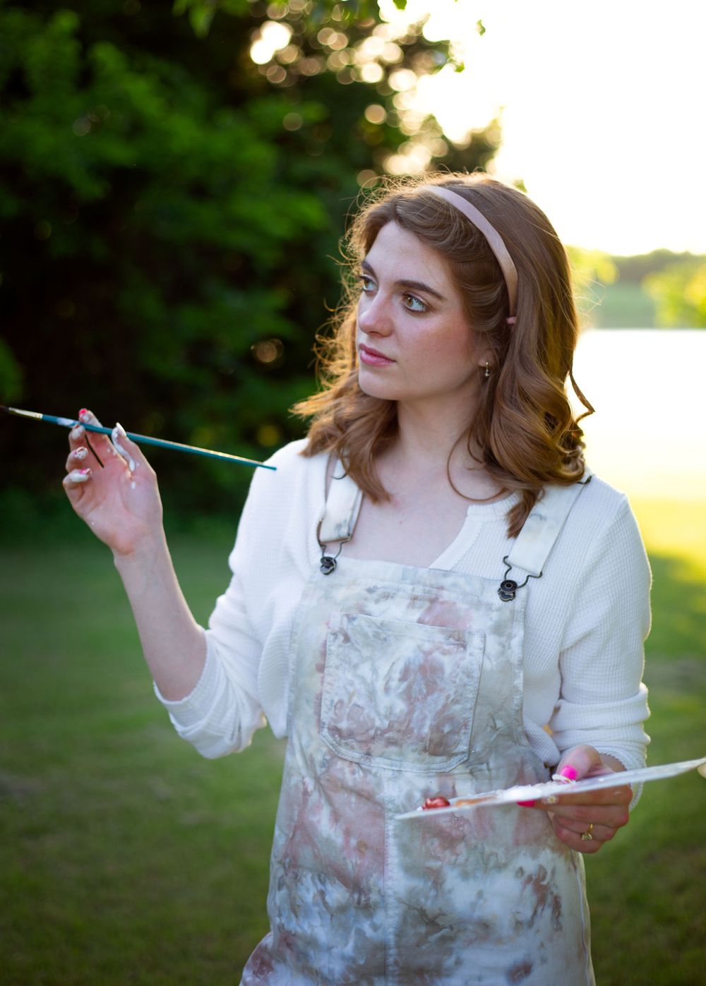 Artist holding paintbrushes while working outdoors in painting overalls.