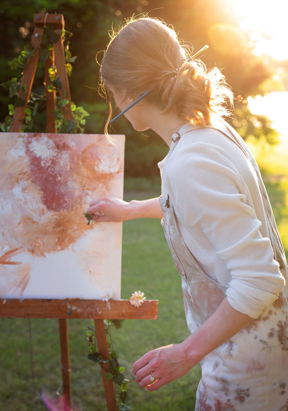 Artist painting on canvas during golden hour in a garden setting.