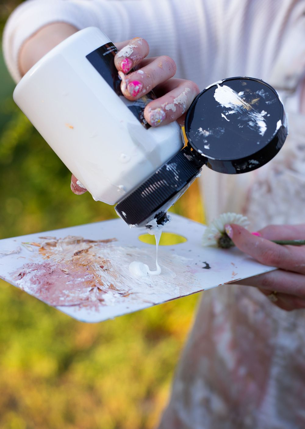 Close-up of hands with floral nail art pouring paint supplies outdoors.