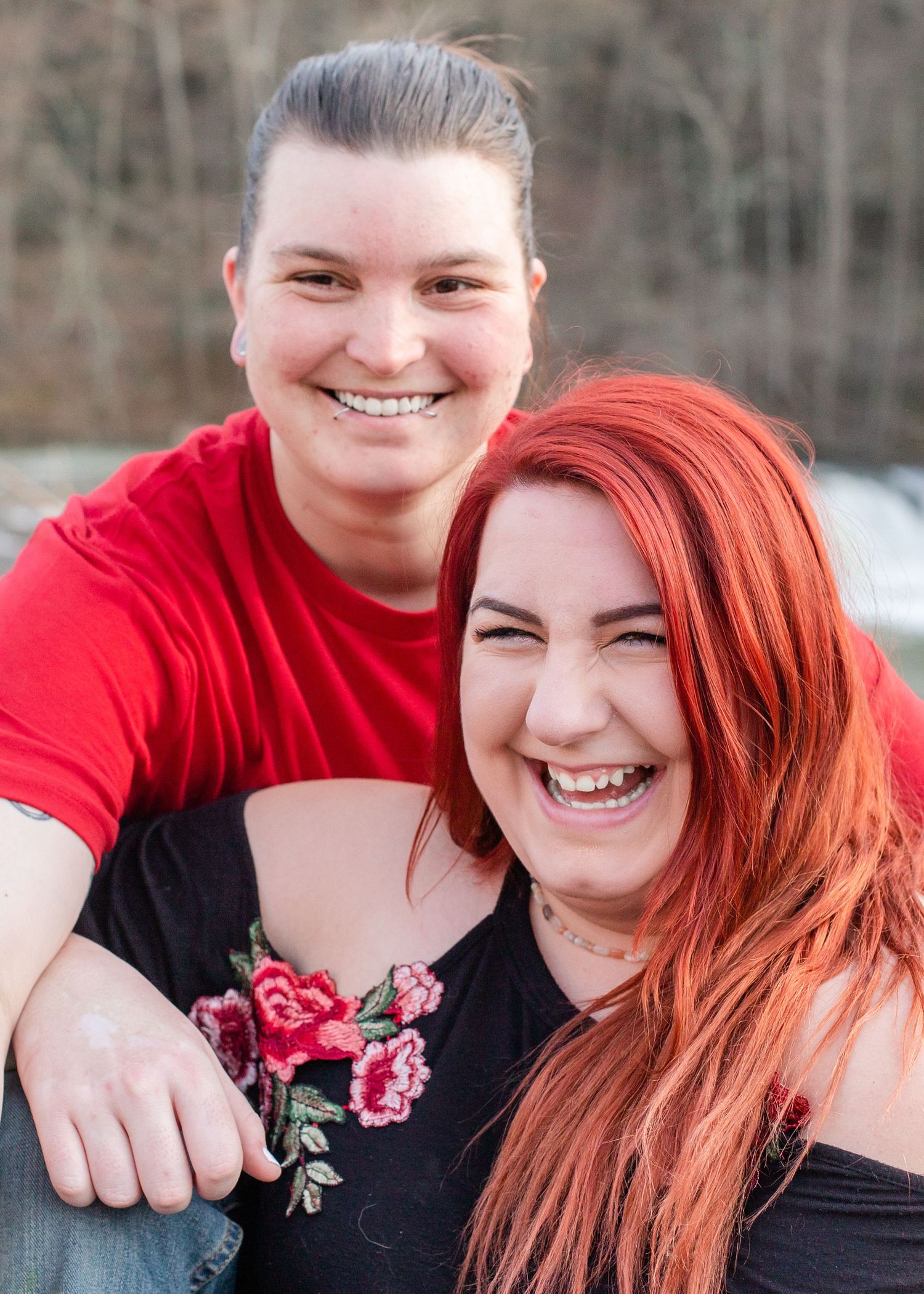 A happy couple embraces while wearing red and black clothing during an outdoor photoshoot.