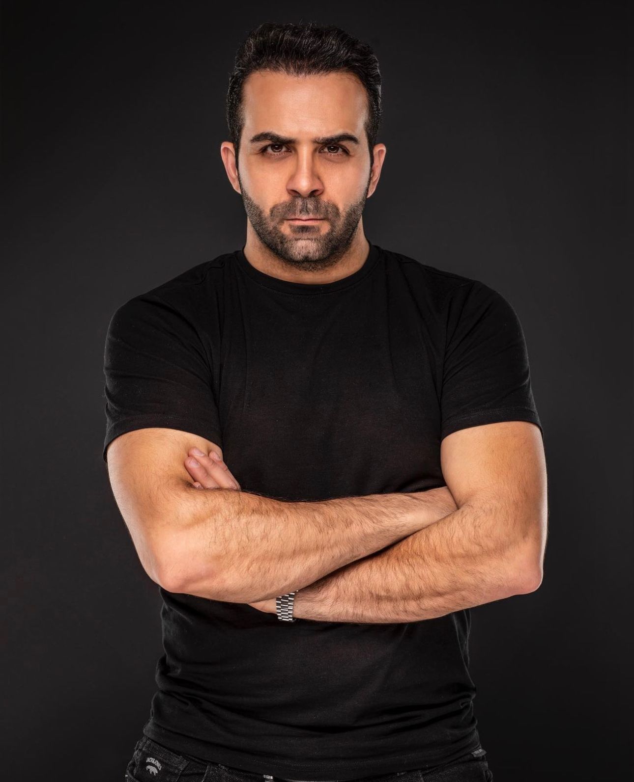 Professional studio portrait of athletic man in black t-shirt against dark background.