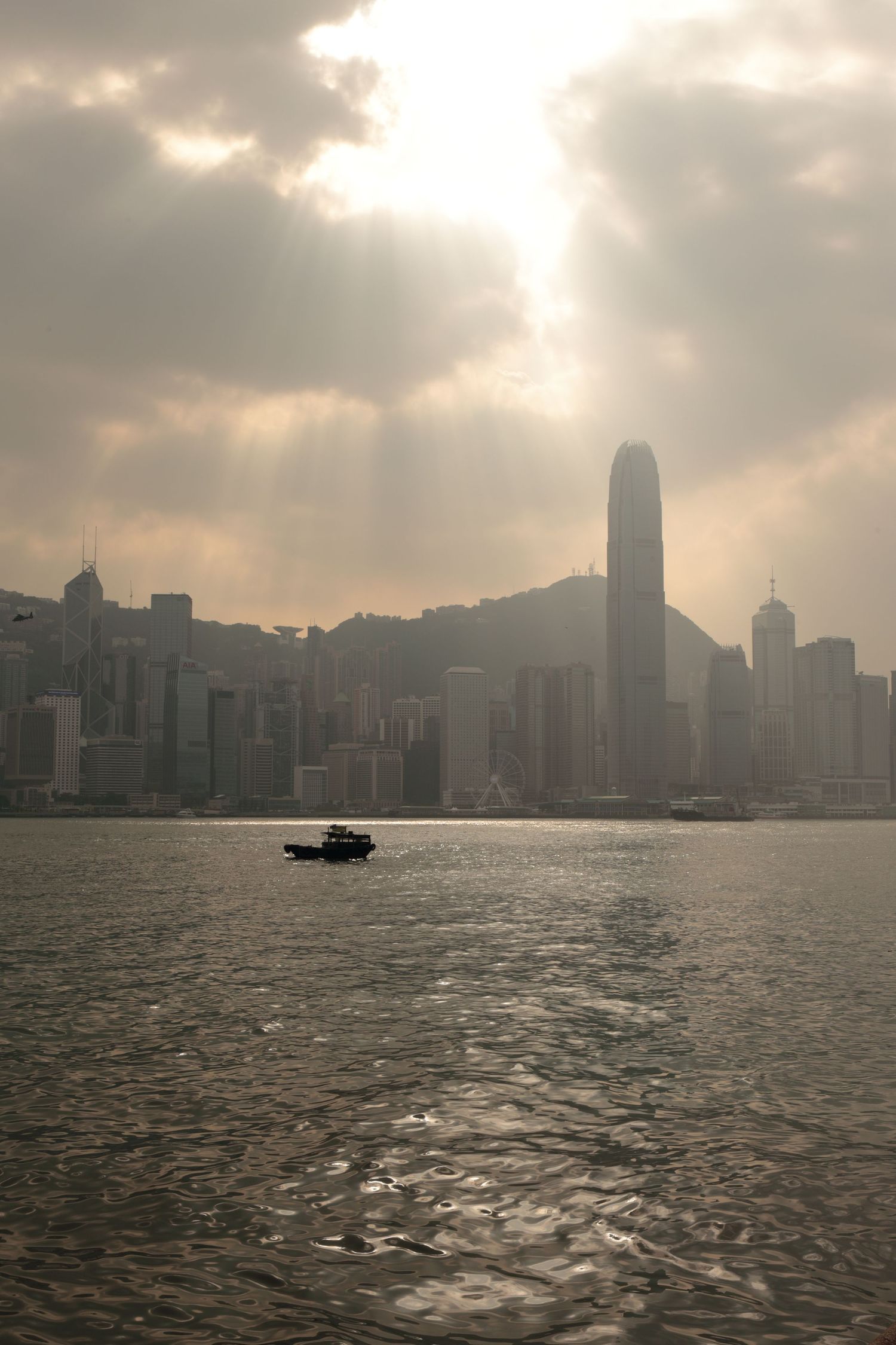 Dramatic sunset view of Hong Kong's Victoria Harbour with sunbeams breaking through clouds.