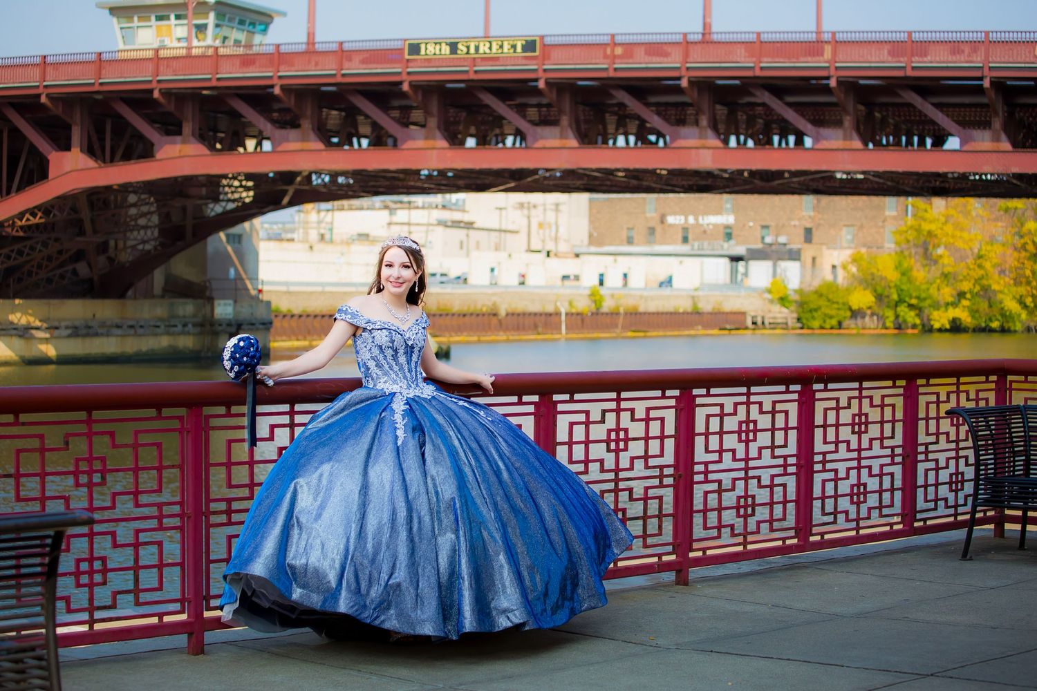 Woman in blue ball gown poses on bridge with red railings during celebration photoshoot.
