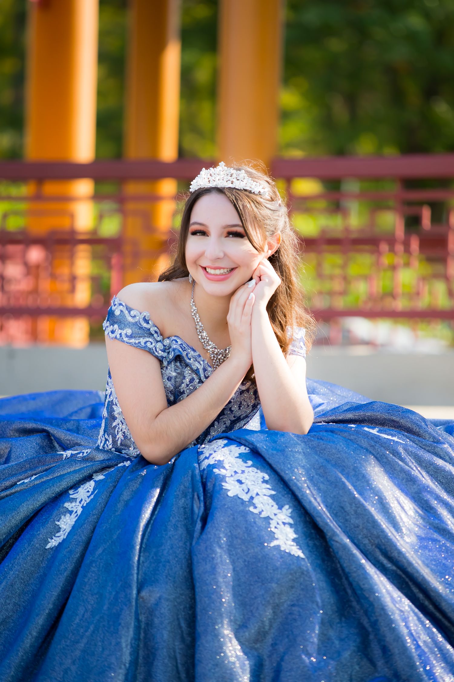 Woman in ornate blue gown and tiara poses gracefully during outdoor portrait session.