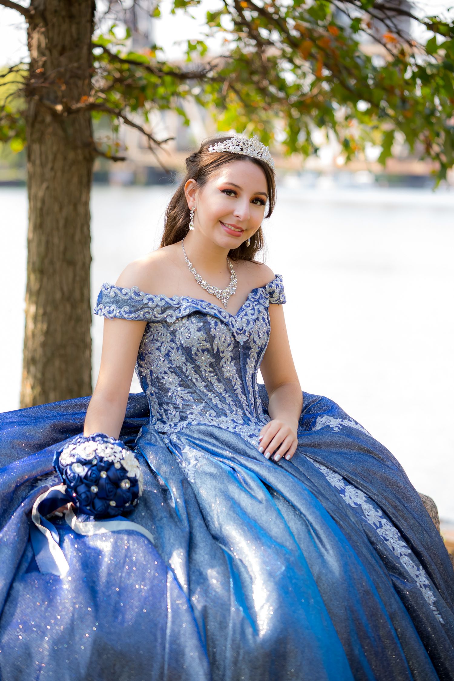 A stunning royal blue quinceañera ball gown with intricate beading and off-shoulder design photographed outdoors.