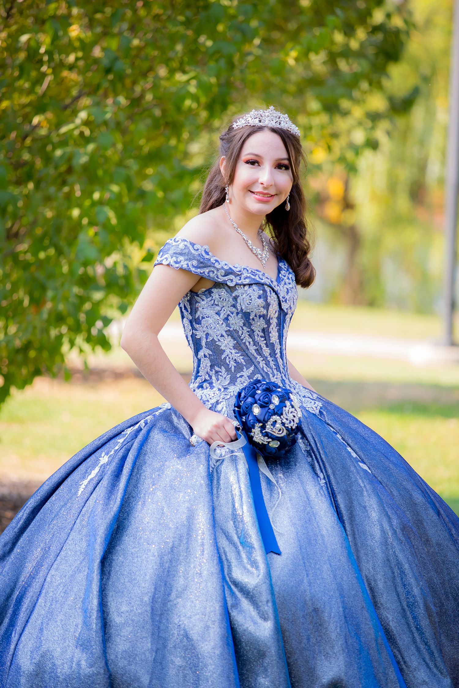 Portrait of woman in sparkly blue quinceañera dress holding navy bouquet.
