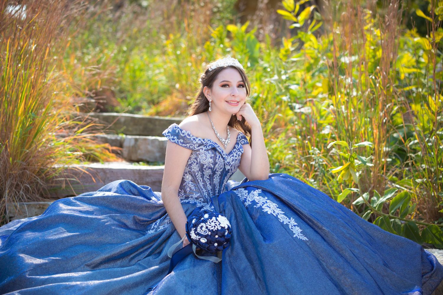 Outdoor portrait featuring a sparkling blue formal gown amidst garden foliage.
