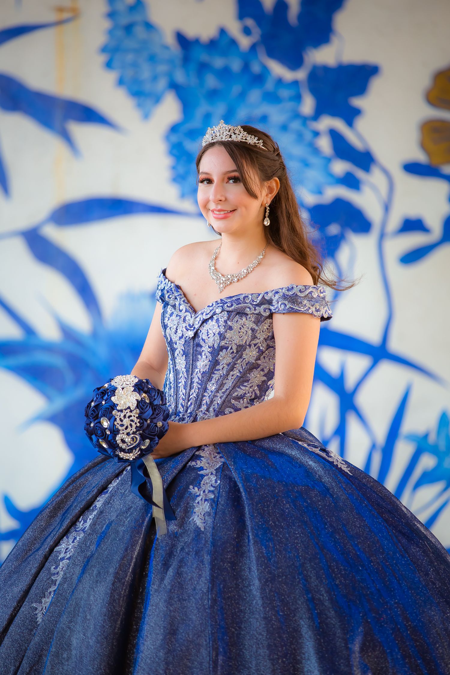 Royal blue ball gown with beaded bodice posed against blue floral wall art.