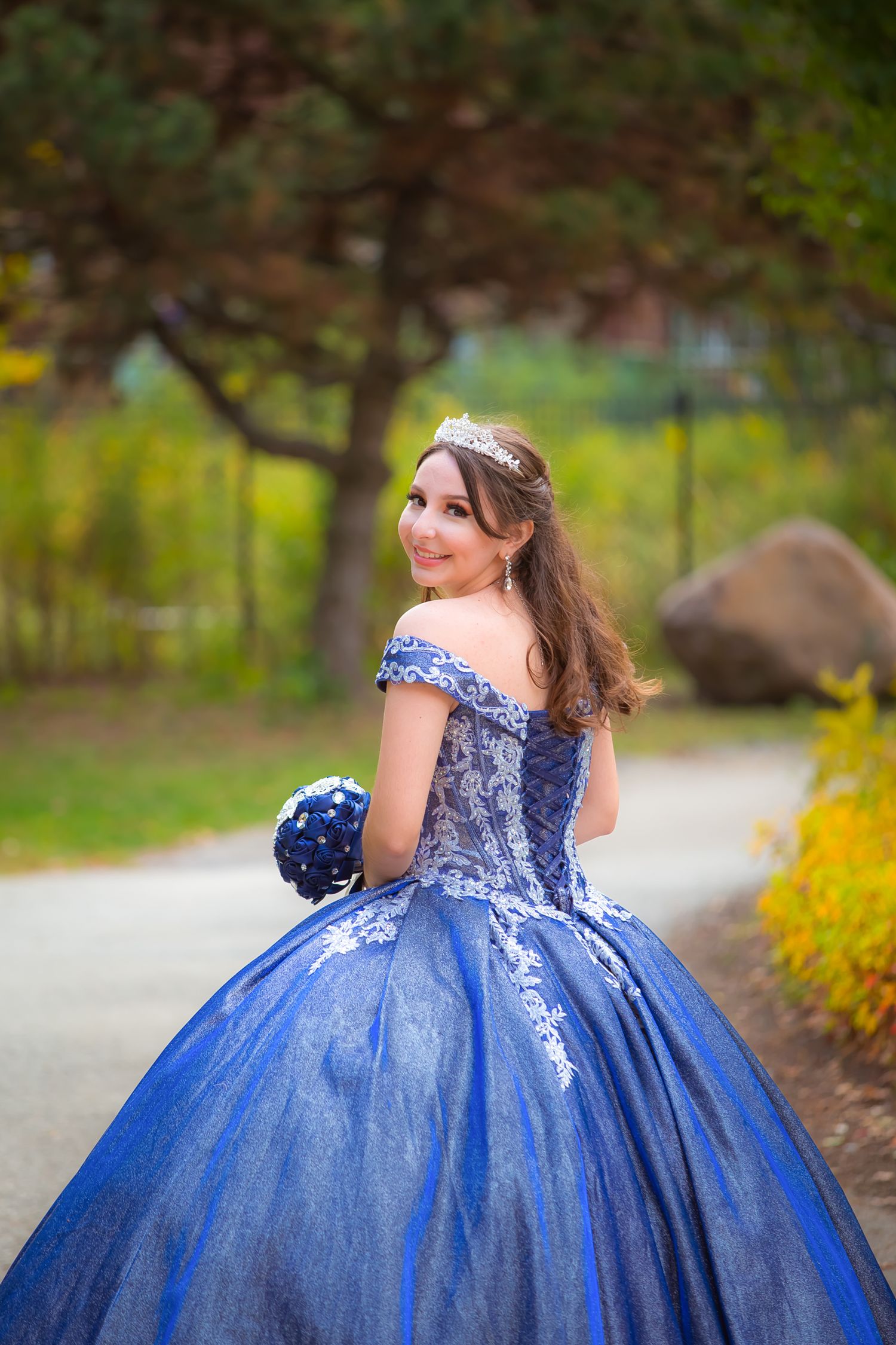 Graceful pose in a royal blue ball gown captured in an autumn garden setting.