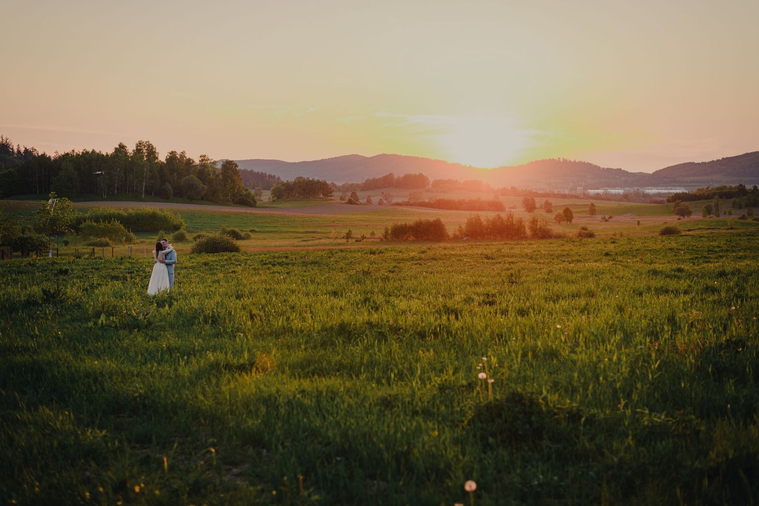 Panoramic sunset landscape over green fields with mountains in the distance.