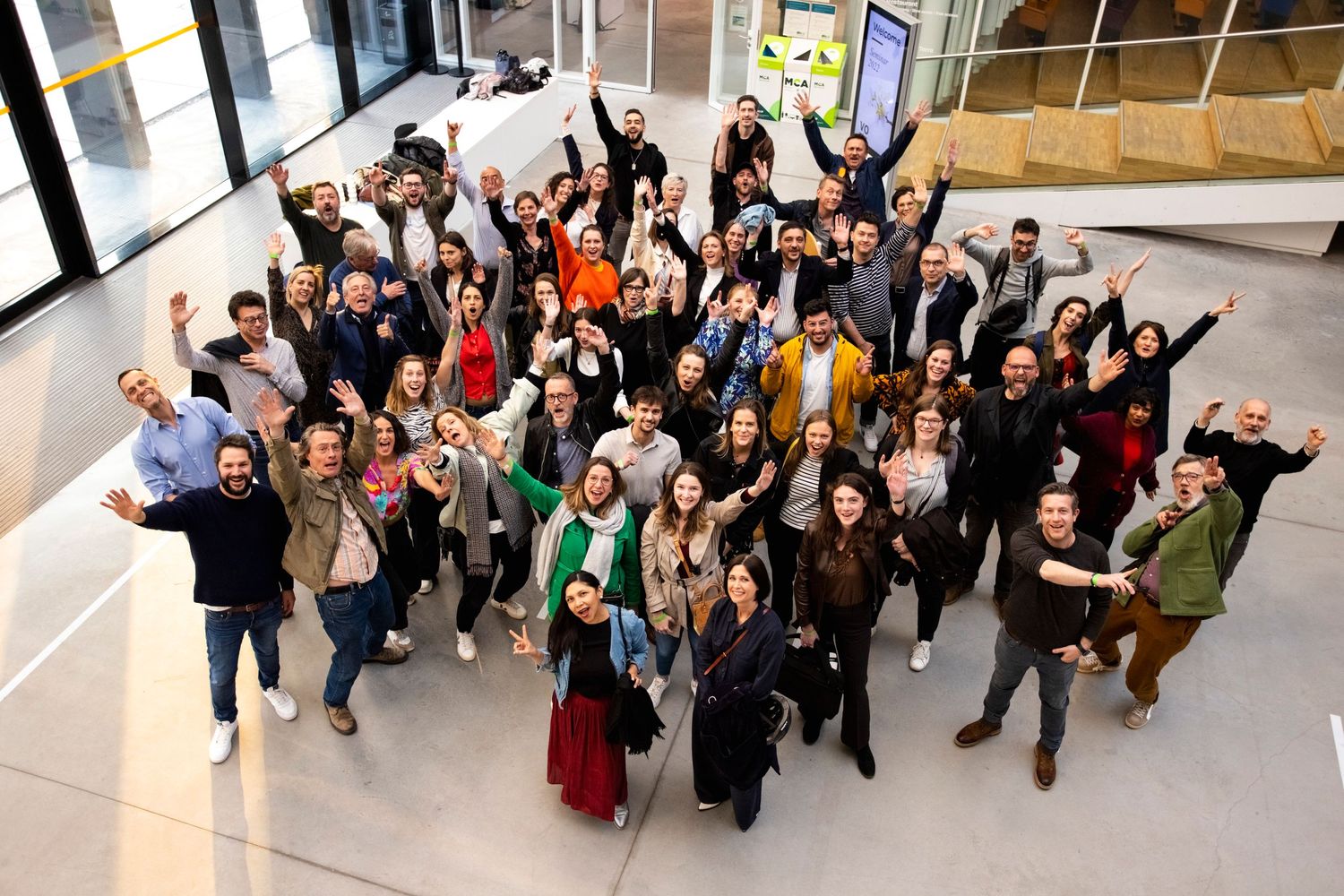 Large group photo of enthusiastic participants posing with raised arms indoors.
