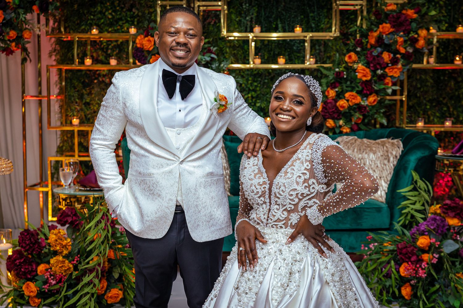 Newlyweds pose in elegant attire surrounded by colorful floral decor.