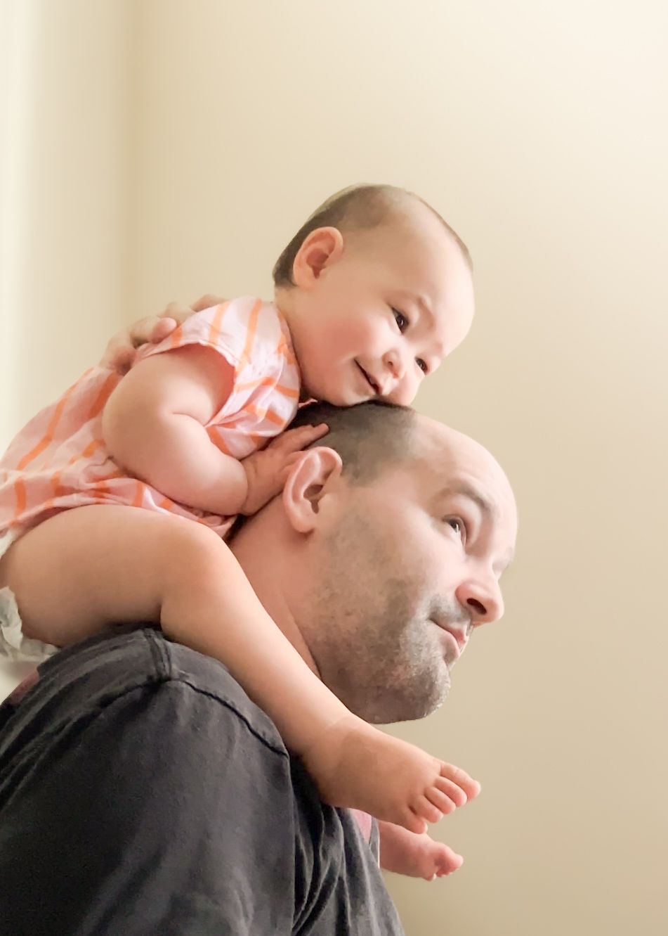 A touching moment of a baby resting on an adult's shoulders while smiling in an indoor setting.