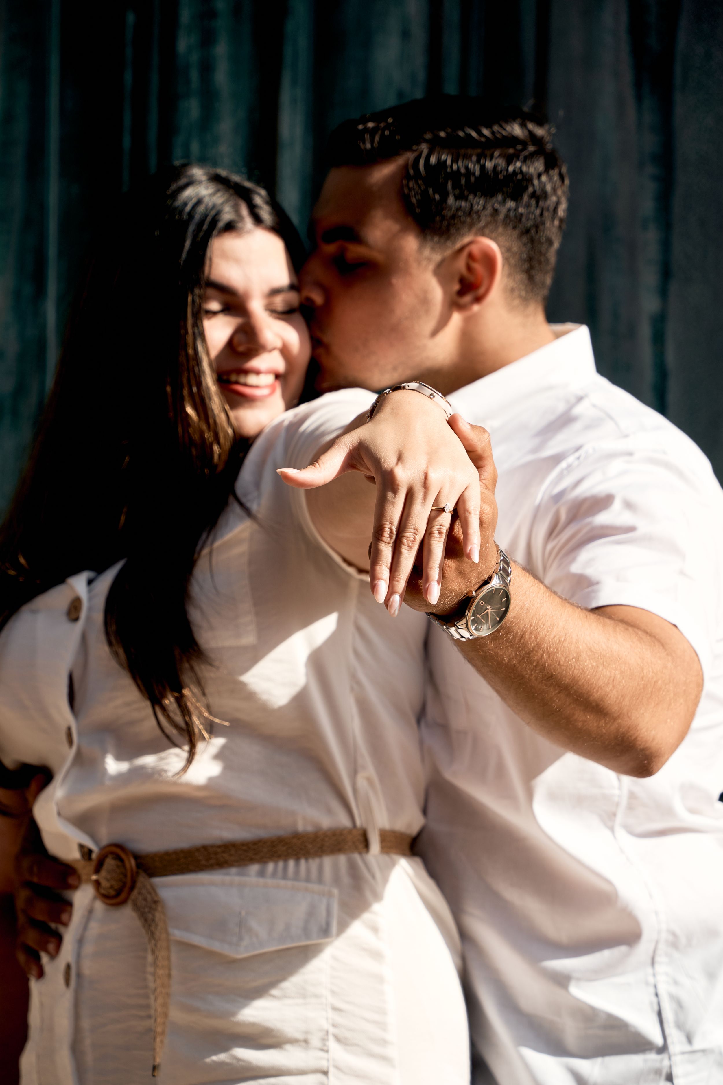 A couple in white clothing embraces in an intimate moment against a dark backdrop.