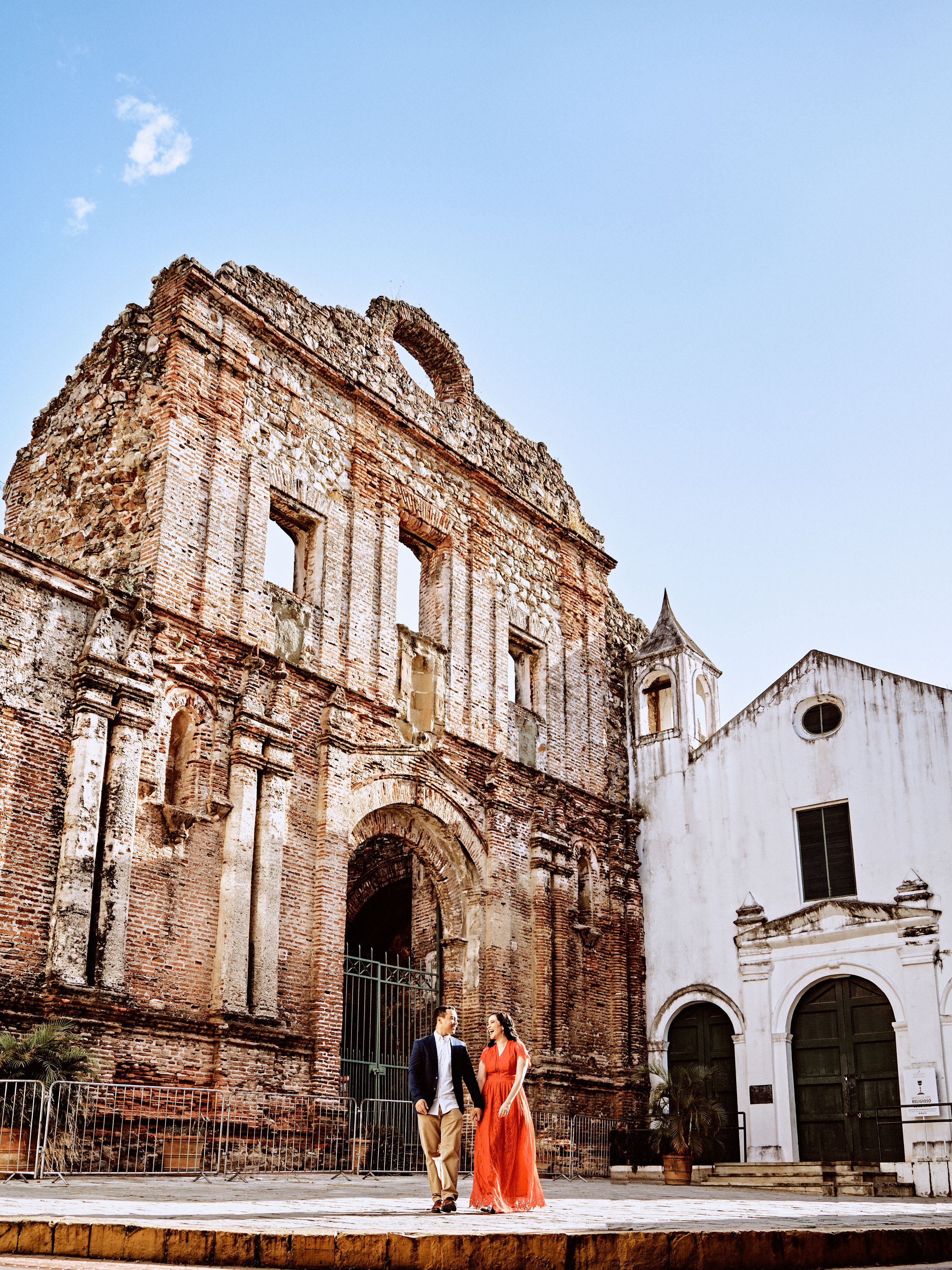 Couple poses in front of historic Spanish colonial ruins and architecture.