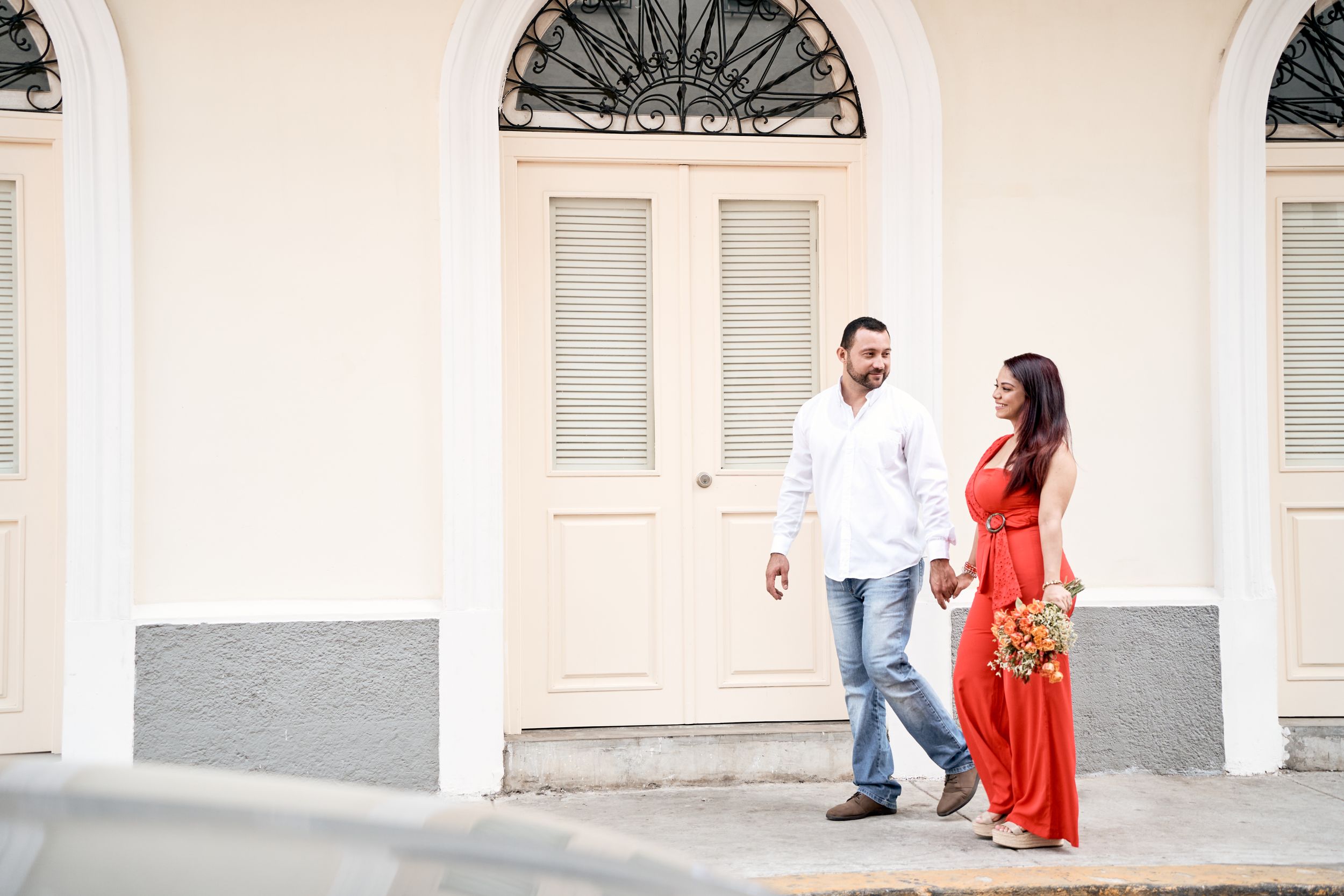 A couple walking and laughing together along a colonial building with white arches.