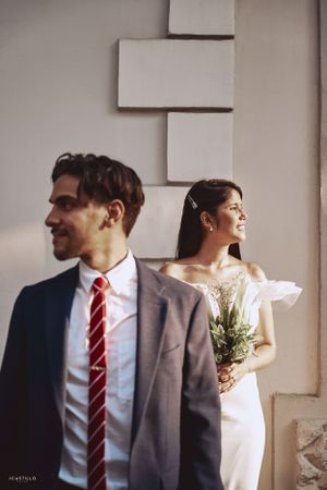 A stylish couple poses separately against a modern white wall backdrop.